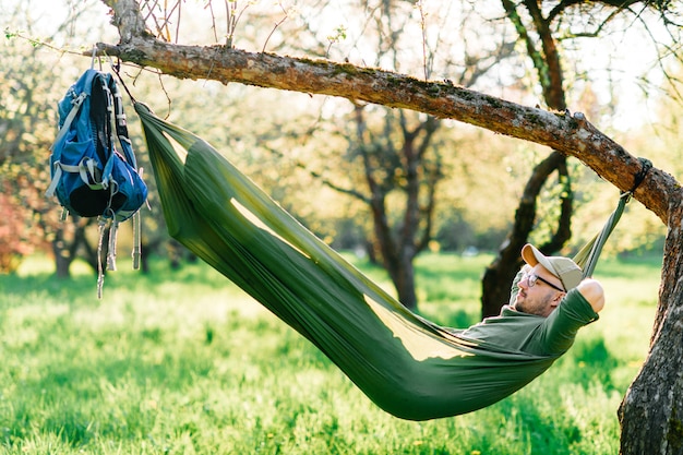 Homem feliz relaxante na rede pendurada na macieira no parque ensolarado de verão.