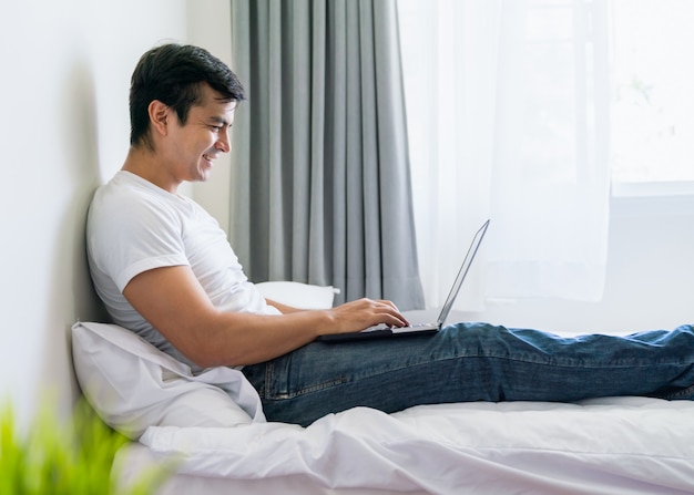 Homem feliz relex usando o laptop na cama no quarto