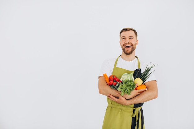 Homem feliz segurando muitos vegetais frescos diferentes no fundo branco