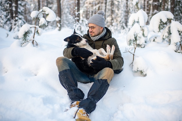 Homem feliz, segurando o cão adorável nas mãos no bosque nevado.