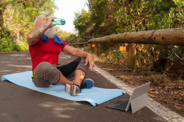 Homem feliz sênior com barba branca bebendo água depois de fazer exercícios ao ar livre na natureza