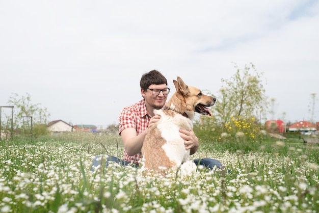 Homem feliz sentado com cão pastor de raça mista na grama verde em flores da primavera