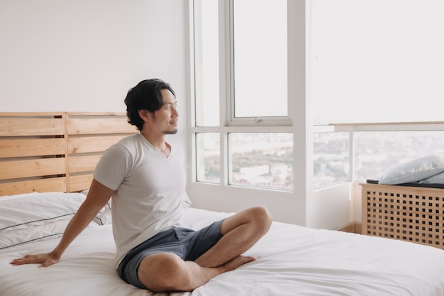 Homem feliz sentado e relaxado em sua cama em seu apartamento