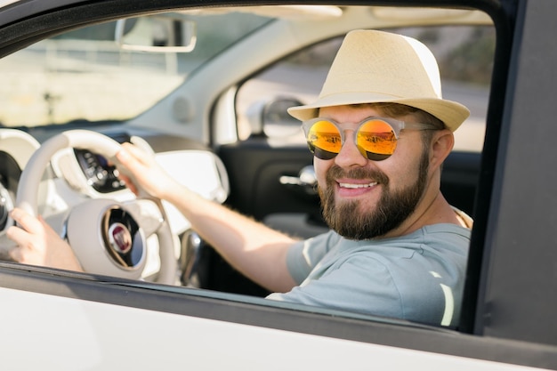 Homem feliz sentado em um carro conversível branco com uma bela vista e se divertindo nas férias de verão e no conceito de aluguel de carro