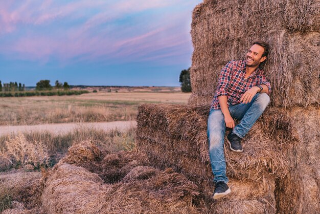 Homem feliz, sentado em uma pilha de feno