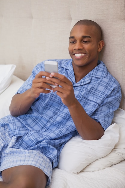 Homem feliz sentado na cama enviando texto