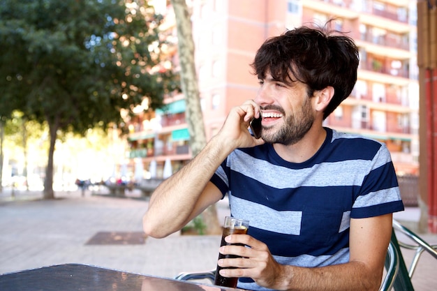 Homem feliz sentado no café ao ar livre e falando no celular