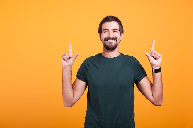 Homem feliz sorrindo e apontando para cima com os dedos. Copyspace disponível para sua promoção de texto e propaganda. Filmado em fundo laranja