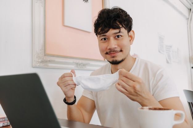 Homem feliz trabalhando em um café tirando a máscara e sorrindo