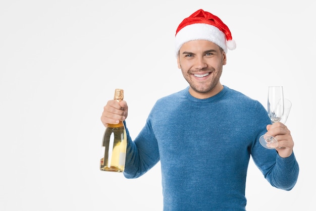 Homem feliz usando chapéu de Papai Noel e segurando taças e garrafa de champanhe sobre fundo branco