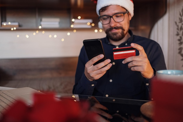 Homem feliz usando chapéu de papai noel segurando presente ou cartão de crédito