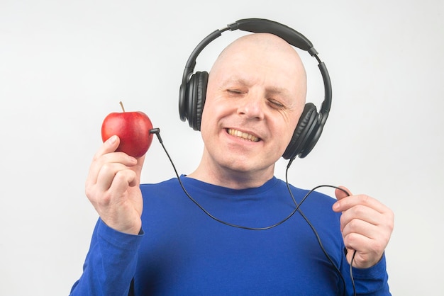 homem feliz usando fones de ouvido portáteis de tamanho normal ouve música usando um player de maçã.