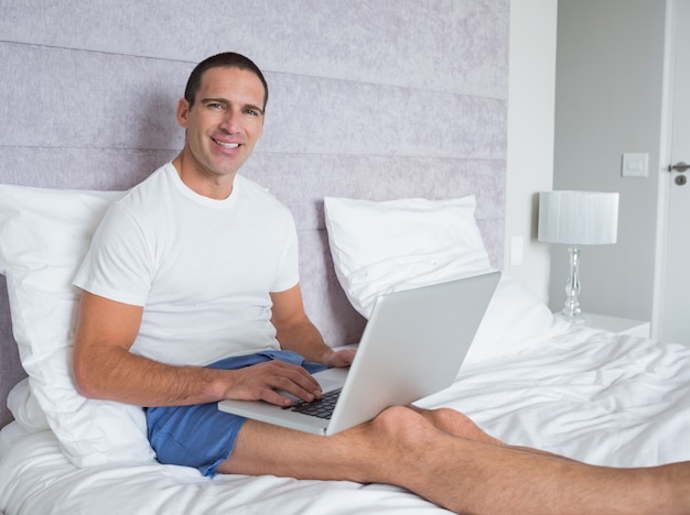 Homem feliz usando o laptop na cama