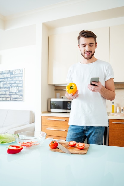 Homem feliz usando smartphone na cozinha