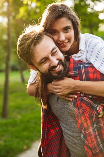 homem feliz vestido com roupa casual dando carona para mulher bonita no parque verde