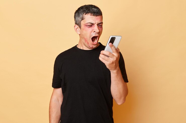 Foto homem ferido agressivo com raiva em camiseta preta com hematomas e abrasões no rosto isolado sobre fundo bege segurando smartphone chamando para a polícia gritando