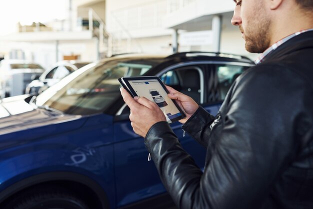 Homem fica dentro do salão do carro com um tablet nas mãos e olha para a imagem do veículo.