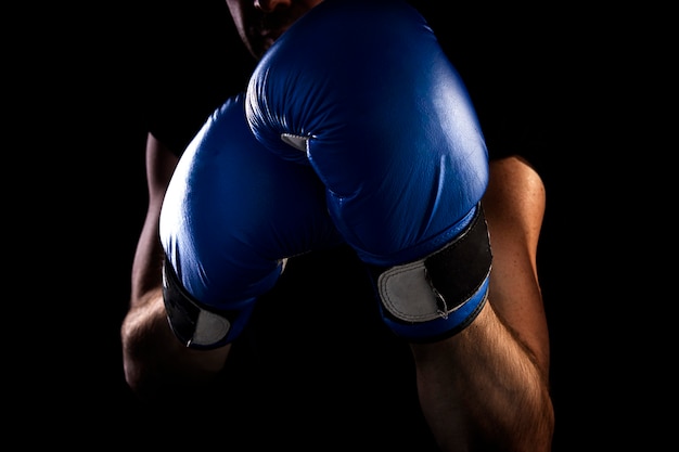 Homem fica em posição de boxe, detém luvas de boxe azuis nas mãos, fundo escuro