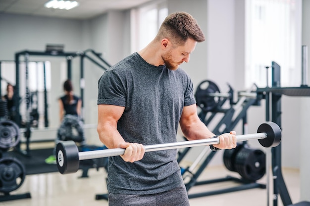 Homem físico atlético treinando na academia de ginástica. Macho bonito forte trabalhando com equipamentos esportivos.