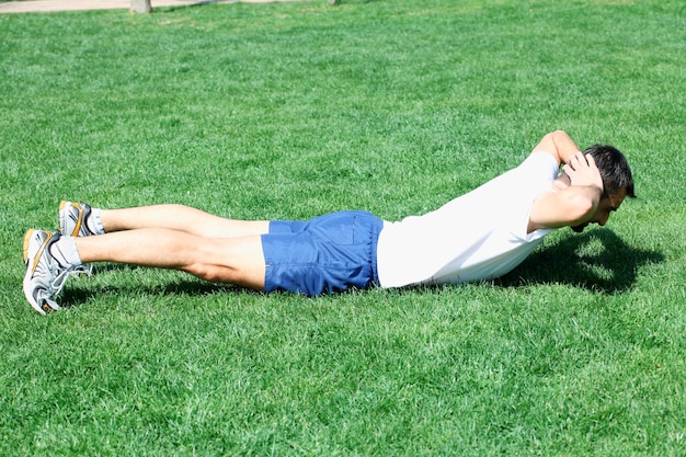 homem fitness exercitando sente-se lá fora na grama no verão.