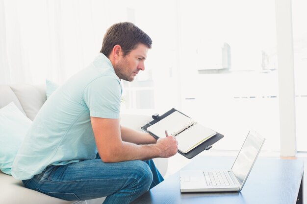 Homem focado em um laptop com um notebook