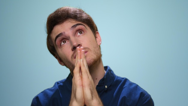 Homem focado fazendo oração no estúdio Cara bonito rezando no fundo azul