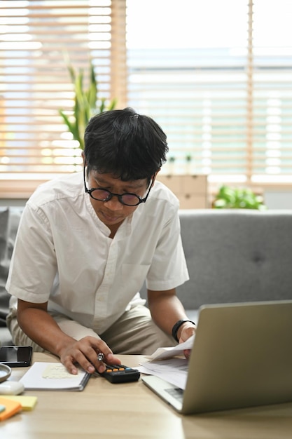 Homem focado usando computador portátil e calculando despesas domésticas Conceito de finanças domésticas