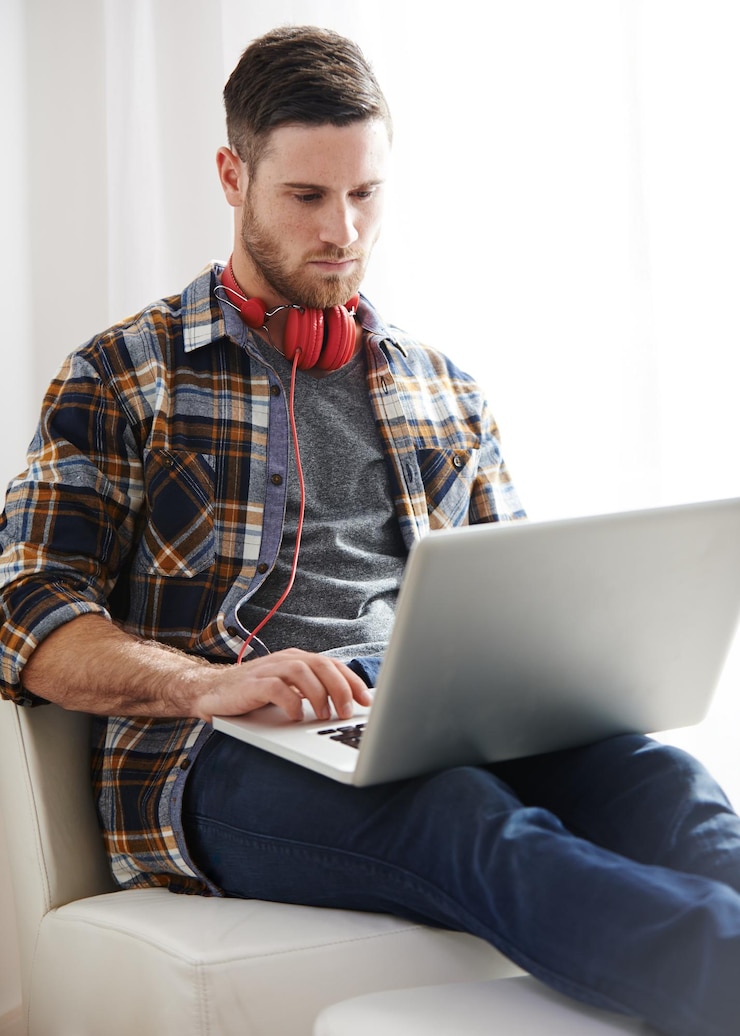 Foto homem fones de ouvido e digitação com laptop em cadeira para software de música criação de áudio ou conteúdo em casa jovem homem ou artista musical com fone de ouvido no computador para trilha sonora digital ou aplicativo