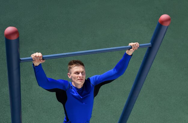 Homem forte atleta fazendo pull-up na barra horizontal sobre o fundo de grama