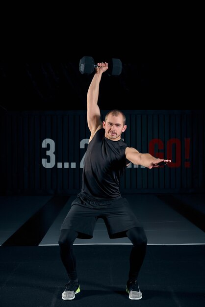 Homem forte e brutal fazendo agachamento com halteres no ginásio, foto de corpo inteiro. Cara fazendo exercícios com halteres dentro de casa. Copie o espaço. Estilo de vida, hobby, interesse