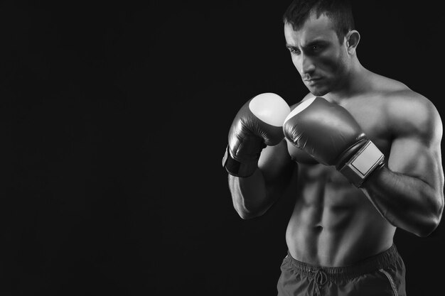 Homem forte e musculoso em luvas de boxe vermelhas no fundo preto do estúdio, discreto, cópia espaço, preto e branco