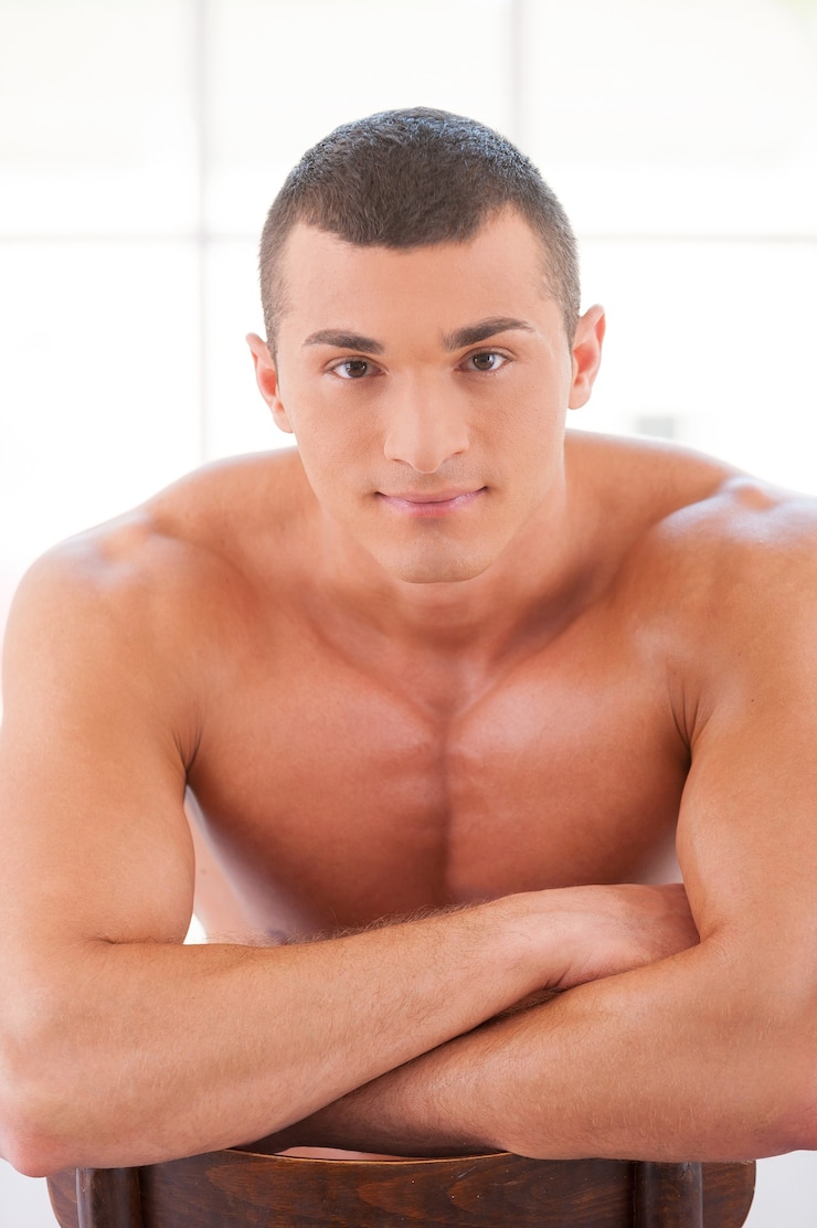 Foto homem forte e musculoso. jovem bonito e musculoso sentado na cadeira olhando para a câmera