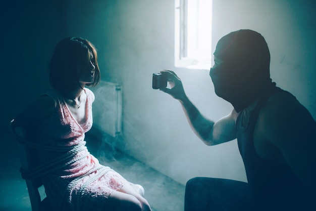 Homem forte e musculoso na máscara preta está segurando o telefone na frente da garota e olhando para ela.