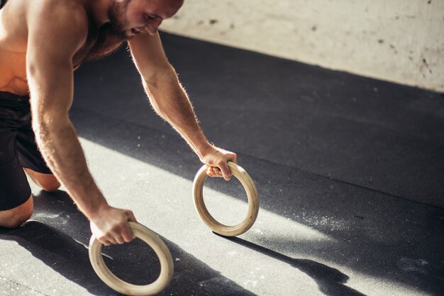 Homem forte está fazendo flexões por anéis.