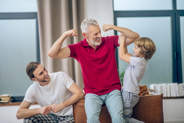 Homem forte. Homem grisalho mostrando seus músculos para seu filho e se sentindo feliz