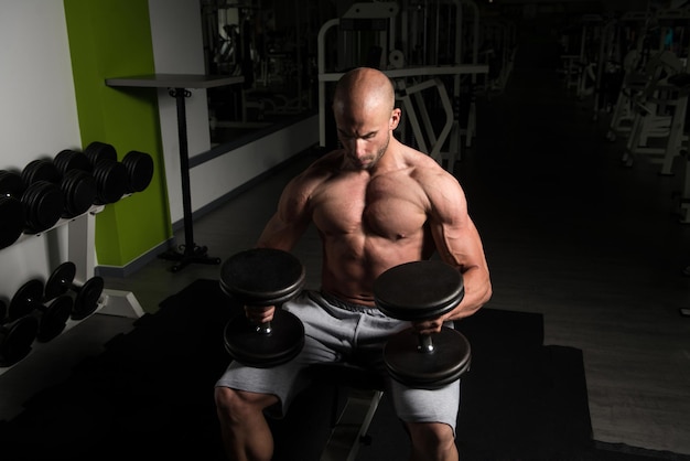 Homem forte na academia e exercitando o peito com halteres Muscular Atlético Fisiculturista Fitness Modelo Exercício