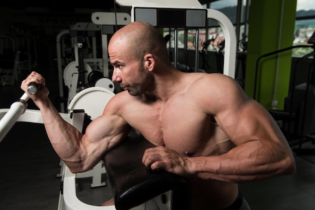 Homem forte na academia exercitando bíceps na máquina Muscular Atlético Fisiculturista Fitness Modelo Exercício