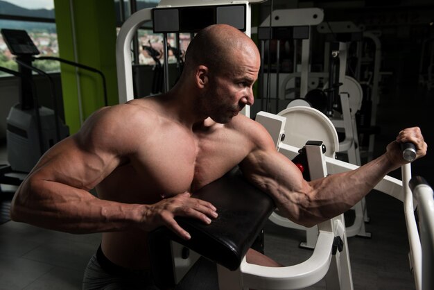 Homem forte na academia exercitando bíceps na máquina Muscular Atlético Fisiculturista Fitness Modelo Exercício