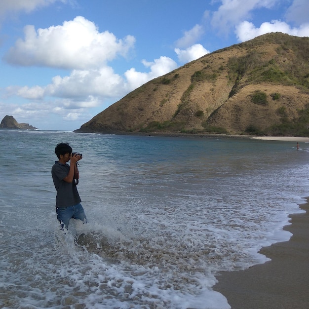 Foto homem fotografando enquanto está de pé na costa contra a montanha