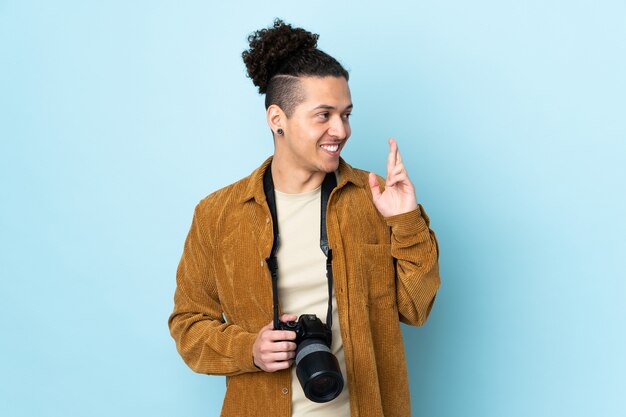 Homem fotógrafo sobre parede azul isolada cruzando os dedos