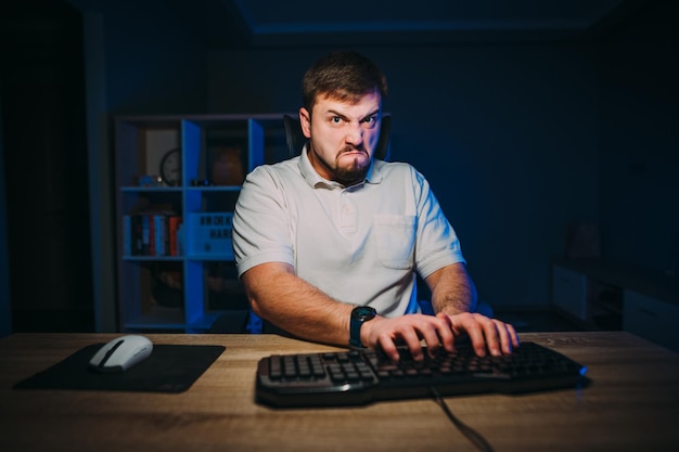 homem freelancer barbudo digitando com raiva no teclado à noite em casa olhando para a câmera