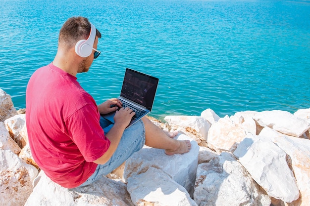 Homem freelancer trabalhando no laptop no banco do porto da cidade no verão