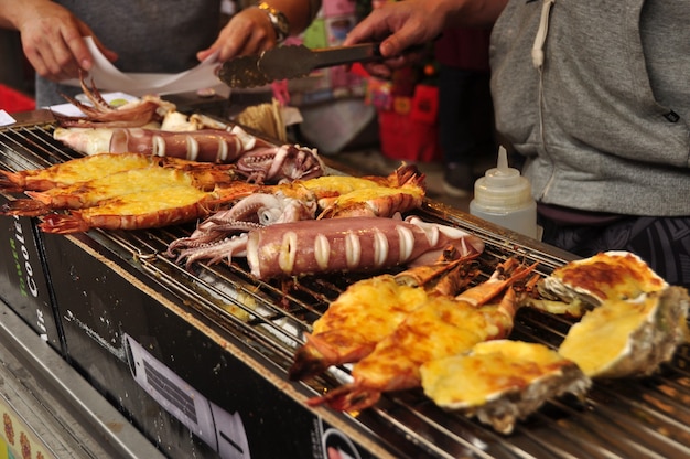 Homem fritando pratos de frutos do mar exóticos para churrasco à venda na rua. Vendedor que frita lula em Hong Kong.