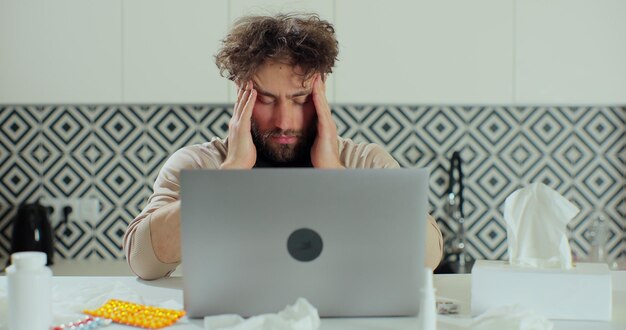 Homem frustrado, sofrendo de dor de cabeça no trabalho em casa. trabalhador tenso exausto lidando com enxaqueca, conceito de estresse emocional sentindo dor sentado na mesa de escritório homa com laptop.