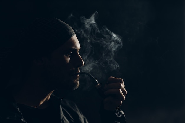 Homem fumando cachimbo em fundo escuro. Retrato de perfil retroiluminado.