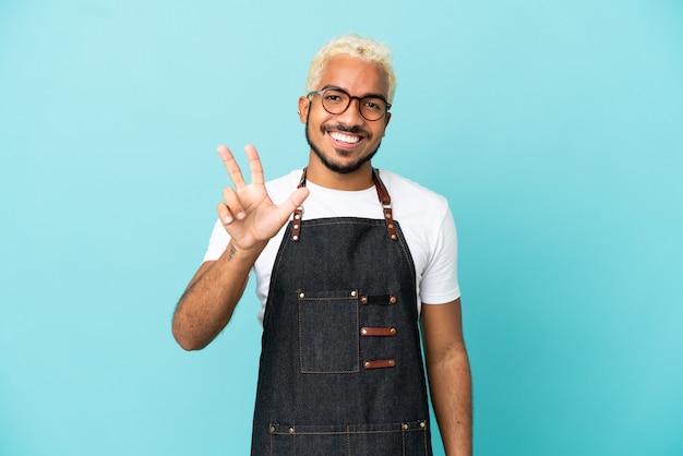 Homem garçom colombiano do restaurante isolado em um fundo azul feliz e contando três com os dedos