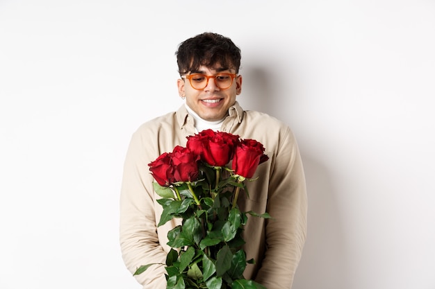 Homem gay alegre recebe rosas vermelhas do namorado, parecendo animado e sorridente, tendo um encontro romântico no dia dos namorados com o amante, em pé sobre um fundo branco.