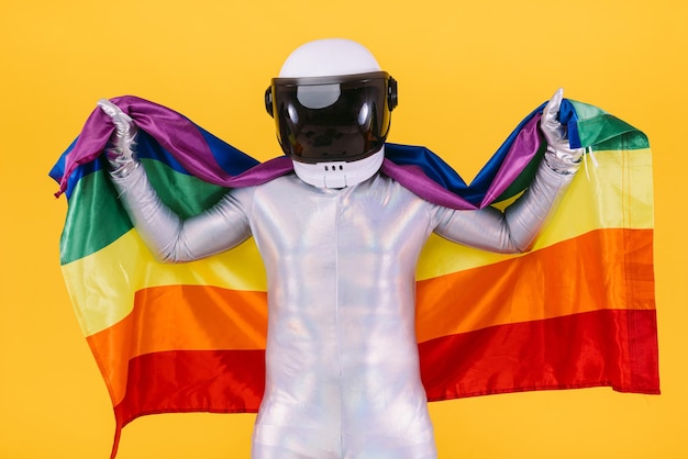 Homem gay vestido de astronauta com capacete e terno prateado segurando uma bandeira do coletivo lgtbi em um fundo amarelo Direitos trans homossexuais gays e conceito de orgulho de gênero