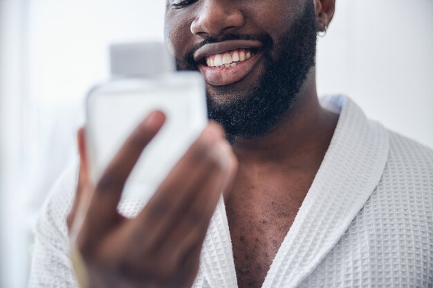 Homem gentil de pele escura se sentindo feliz enquanto se prepara para um encontro romântico, vestindo roupão de banho