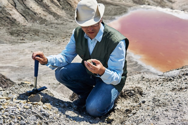 Homem geólogo em uma área deserta examina uma amostra de rocha contra o pano de fundo de um lago salgado colorido